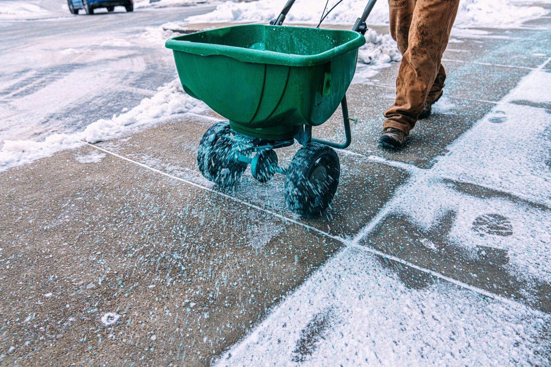 Snow Removal Company or Maintenance Worker spreading Ice-Melting Calcium Chloride Salt on a Sidewalk in a Small Business Park / Downtown Area